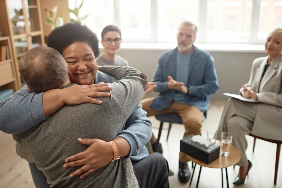 Two people embracing in a group therapy session