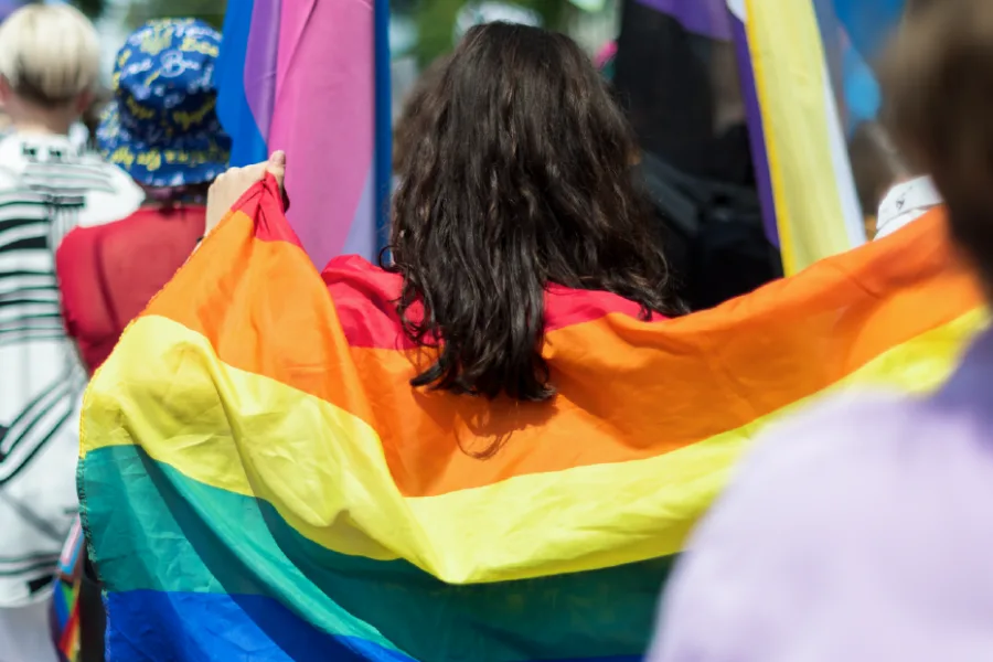A person wearing a rainbow Pride flag at a parade