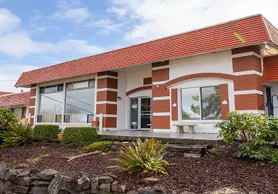 Single-story brick building with a red roof and large front windows, surrounded by landscaped shrubs and rocks.