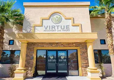Facade of Virtue Recovery Las Vegas treatment center, with double glass doors, stone columns, and a sign reading 'Virtue Recovery Las Vegas' above the entrance; palm trees frame the building.
