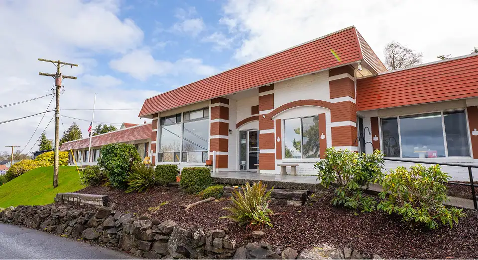 Single-story brick commercial building with a red-tiled roof and large front windows, landscaped with shrubs and a stone wall in front.