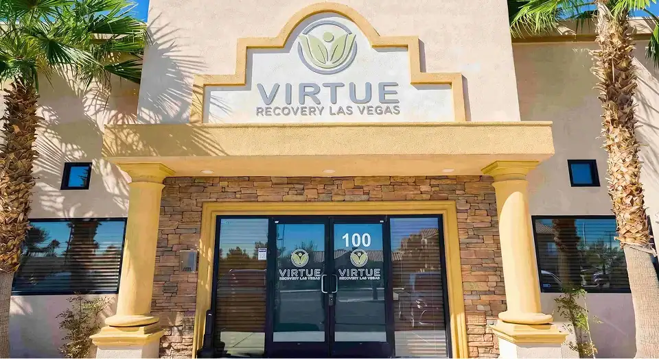 Front of Virtue Recovery Las Vegas center with stone facade, beige columns, palm trees, and glass doors displaying 100.