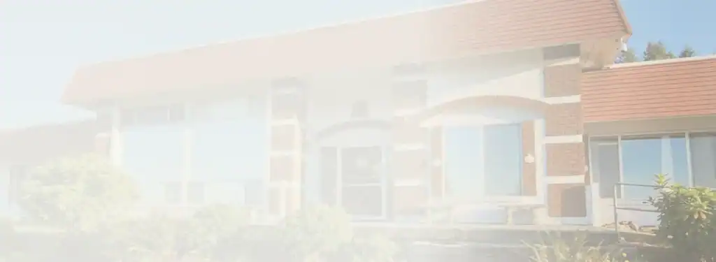 Exterior view of a brick-and-glass commercial building with arched entry and surrounding shrubs in daylight