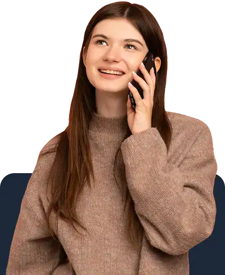 A young woman with long brown hair, wearing a beige sweater, smiles while holding a phone to her ear and looking upward.
