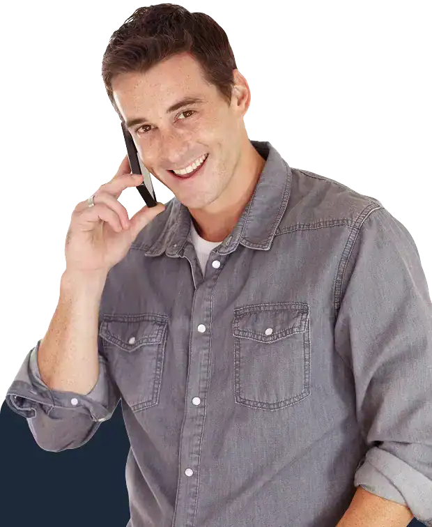 Smiling man in a gray denim shirt talking on a cellphone