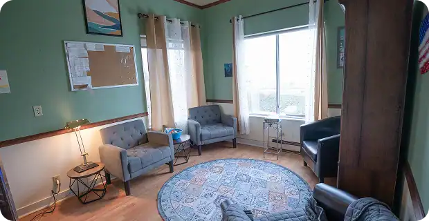 Cozy waiting room with green walls, four blue armchairs, a round patterned rug, and a windowed wall area.